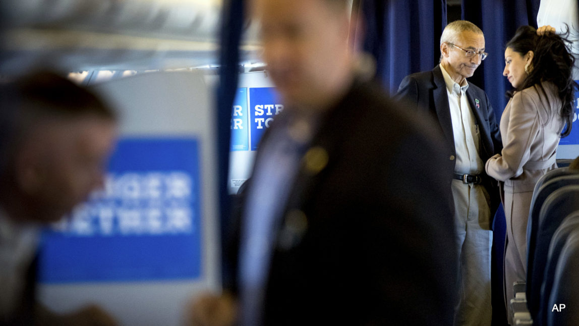 Hillary Clinton's campaign manager John Podesta, second from right, pauses while speaking with senior aide Huma Abedin aboard Clinton's campaign plane while traveling to Miami, Tuesday, Oct. 11, 2016, for a rally.