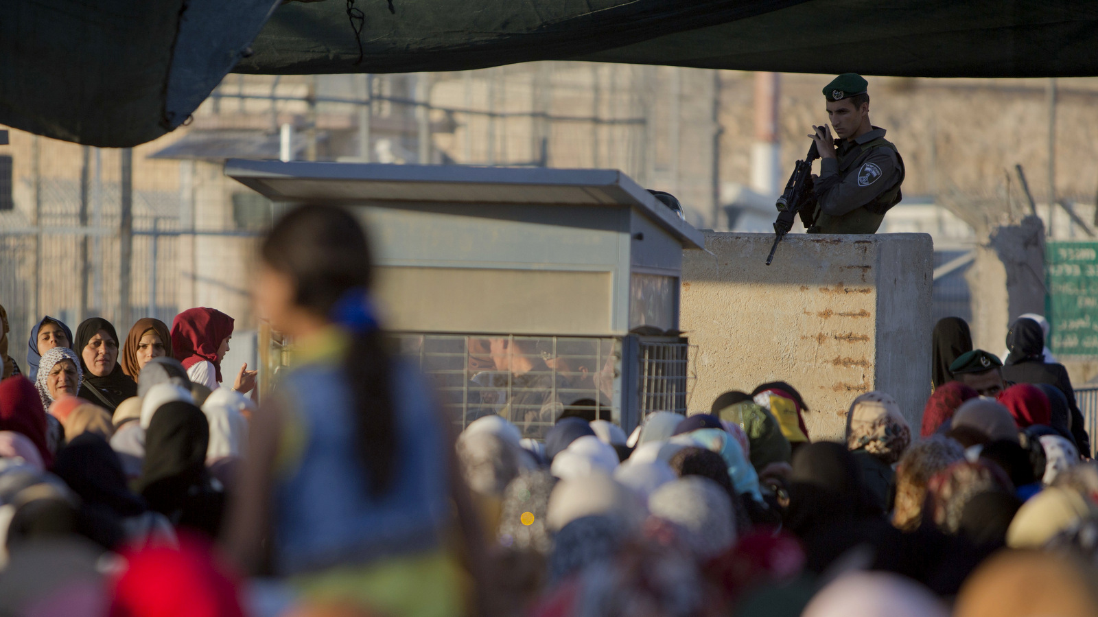 An Israeli border police officer stands as Palestinian women wait to cross the Qalandia checkpoint between the West Bank city of Ramallah and Jerusalem, June 17, 2015. (AP Photo/Majdi Mohammed)