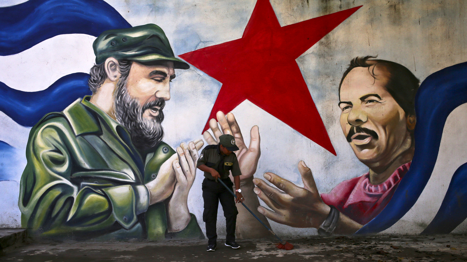 A woman sweeps the Cuba Plaza backdropped by a mural depicting Cuba's former President Fidel Castro and Nicaragua's President Daniel Ortega, in Managua, Nicaragua, Friday, Nov. 4, 2016. (AP Photo/Esteban Felix)
