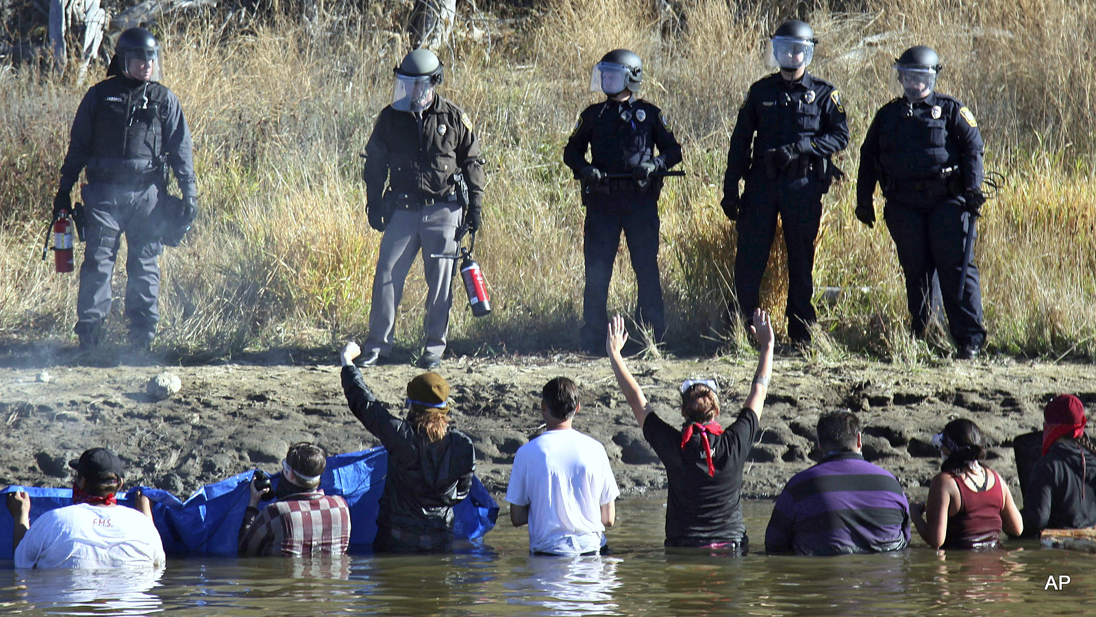 Dozens of protestors demonstrating against the expansion of the Dakota Access Pipeline wade in cold creek waters confronting local police, as remnants of pepper spray waft over the crowd near Cannon Ball, N.D., Wednesday, Nov. 2, 2016. 