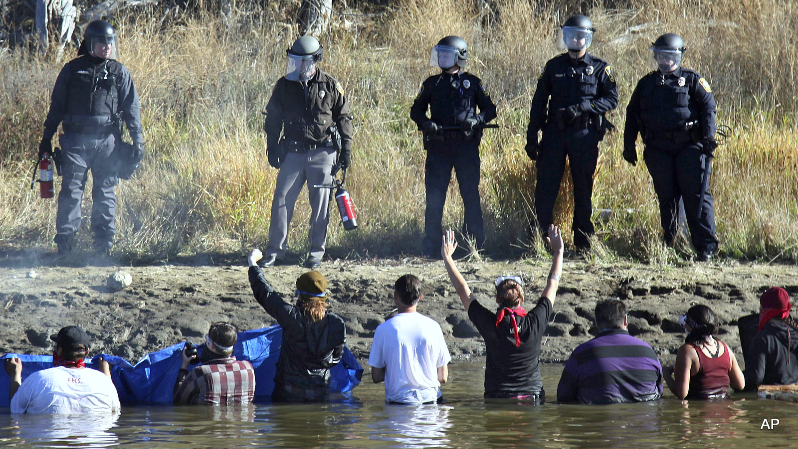 Dozens of protestors demonstrating against the expansion of the Dakota Access Pipeline wade in cold creek waters confronting local police, as remnants of pepper spray waft over the crowd near Cannon Ball, N.D., Wednesday, Nov. 2, 2016.