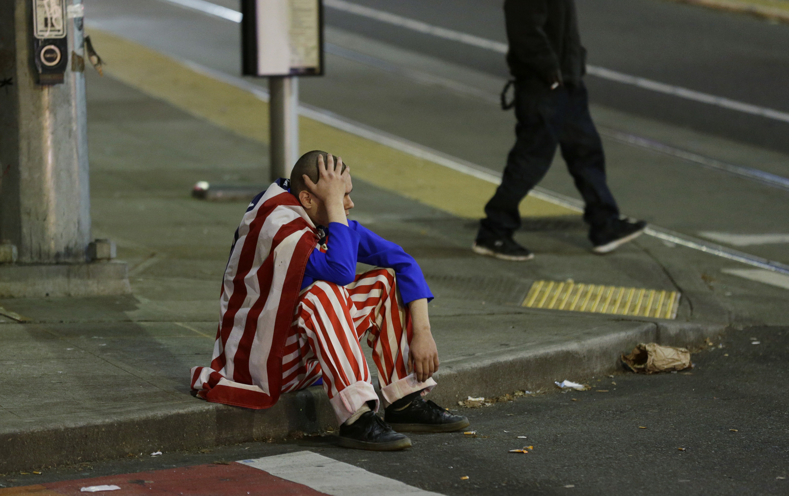 A man dressed in red-white-and-blue sits on the curb during a protest against President-elect Donald Trump, Wednesday, Nov. 9, 2016, in Seattle's Capitol Hill neighborhood. (AP Photo/Ted S. Warren)