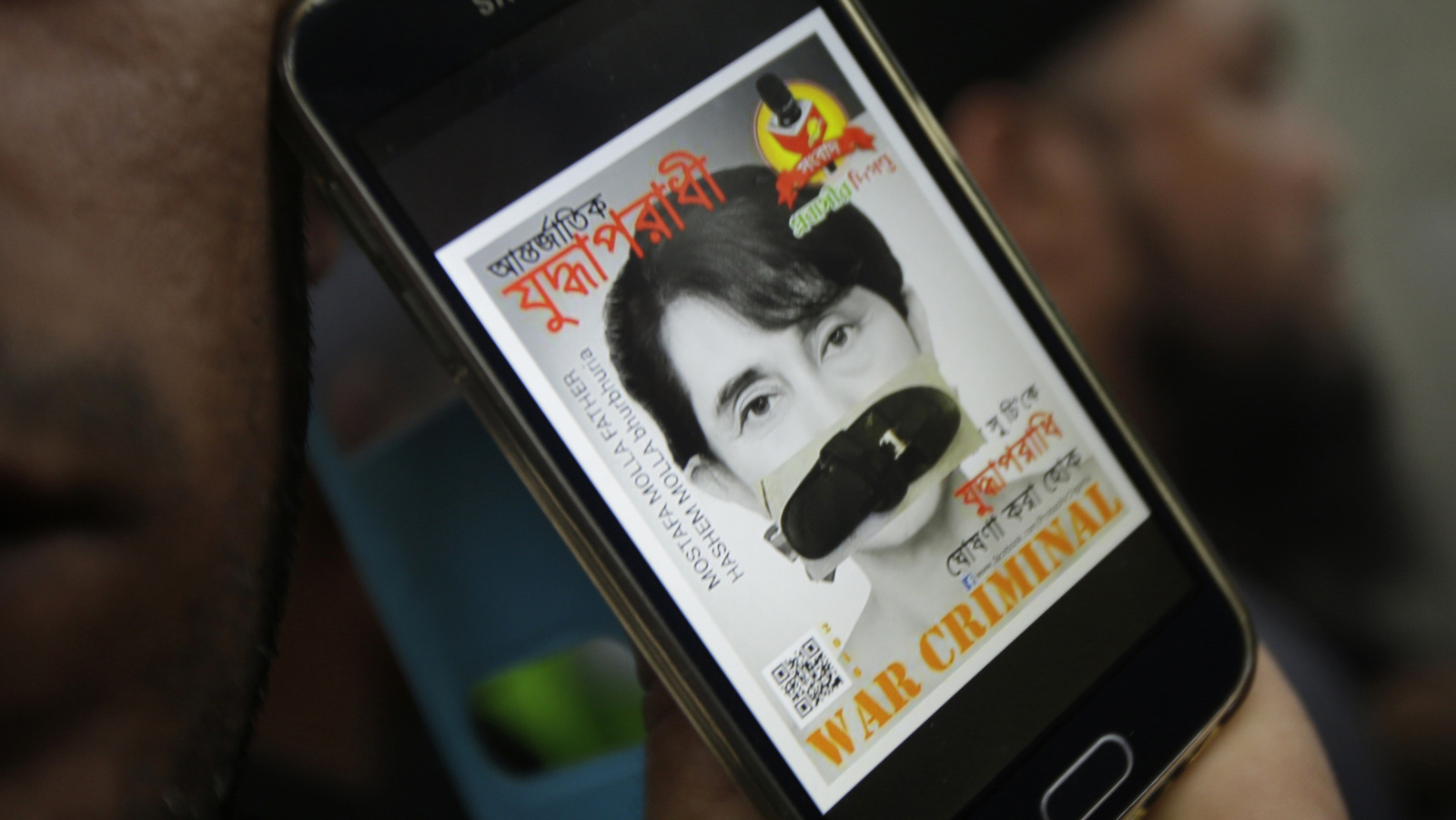 A portrait of Myanmar's Foreign Minister Aung San Suu Kyi with her mouth covered with a sandal displayed on a mobile phone screen is shown by a protester during a demonstration in front of the Myanmar Embassy in Bangkok, Thailand, Friday, Nov. 25, 2016 against the murder, displacement and persecution of Muslim Rohingya in Myanmar. (AP Photo/Sakchai Lalit)