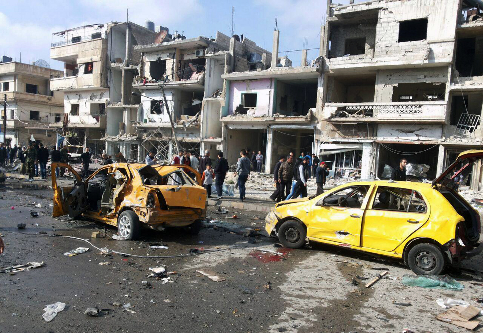 Syrian citizens gather at the scene where two blasts exploded in the pro-government neighborhood of Zahraa, in Homs province, Syria, Sunday, Feb. 21, 2016. Two blasts in the central Syrian city of Homs killed more than a dozen people and injured many others in a wave of violence. (SANA via AP)