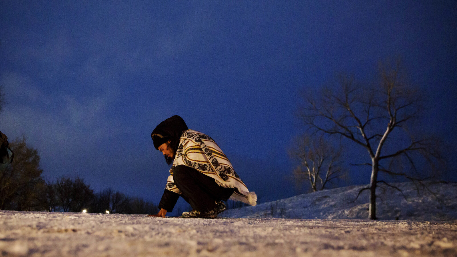 Sean Ptolomek, of Los Angeles, prays while touching the road leading to the Dakota Access oil pipeline site following a demonstration near Cannon Ball, N.D., Wednesday, Nov. 30, 2016. The pipeline is designed to carry oil from North Dakota to Illinois. Opponents, including the Standing Rock Sioux tribe, say it will harm drinking water and cultural sites. (AP Photo/David Goldman)