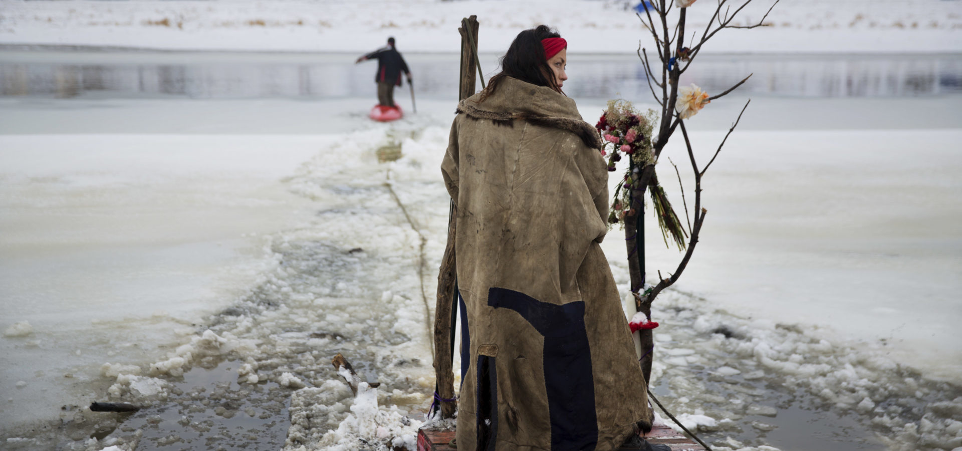 Cat Bigney, part of the Oglala Native American tribe, waits on the shore of the Cannonball river for travelers to arrive by canoe at the Oceti Sakowin camp where people have gathered to protest the Dakota Access oil pipeline in Cannon Ball, N.D. So far, those at the camp have shrugged off the heavy snow, icy winds and frigid temperatures. But if they defy next week's government deadline to abandon the camp, demonstrators know the real deep freeze lies ahead. Life-threatening wind chills and towering snow drifts could mean the greatest challenge is simple survival. Dec. 1, 2016 photo, (AP Photo/David Goldman)