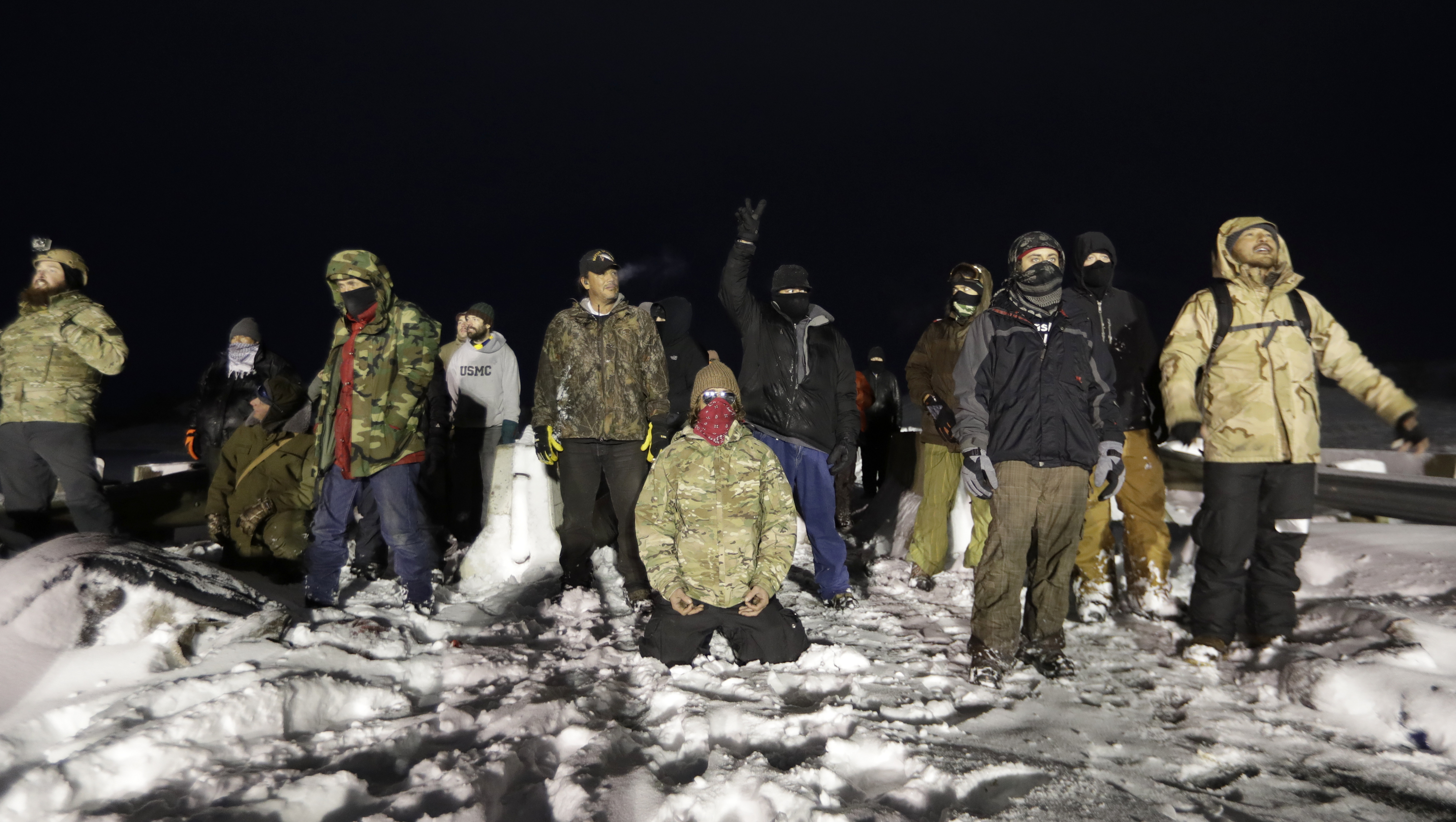 Military veterans stand on a closed bridge to protest across from police protecting the Dakota Access oil pipeline site in Cannon Ball, N.D., Thursday, Dec. 1, 2016. (AP Photo/David Goldman)
