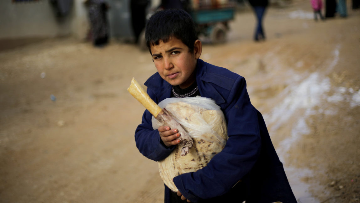 A Syrian boy displaced with his family from eastern Aleppo holds a sandwich and bread bag in the village of Jibreen south of Aleppo, Syria, Saturday, Dec. 3, 2016. (AP Photo/Hassan Ammar)