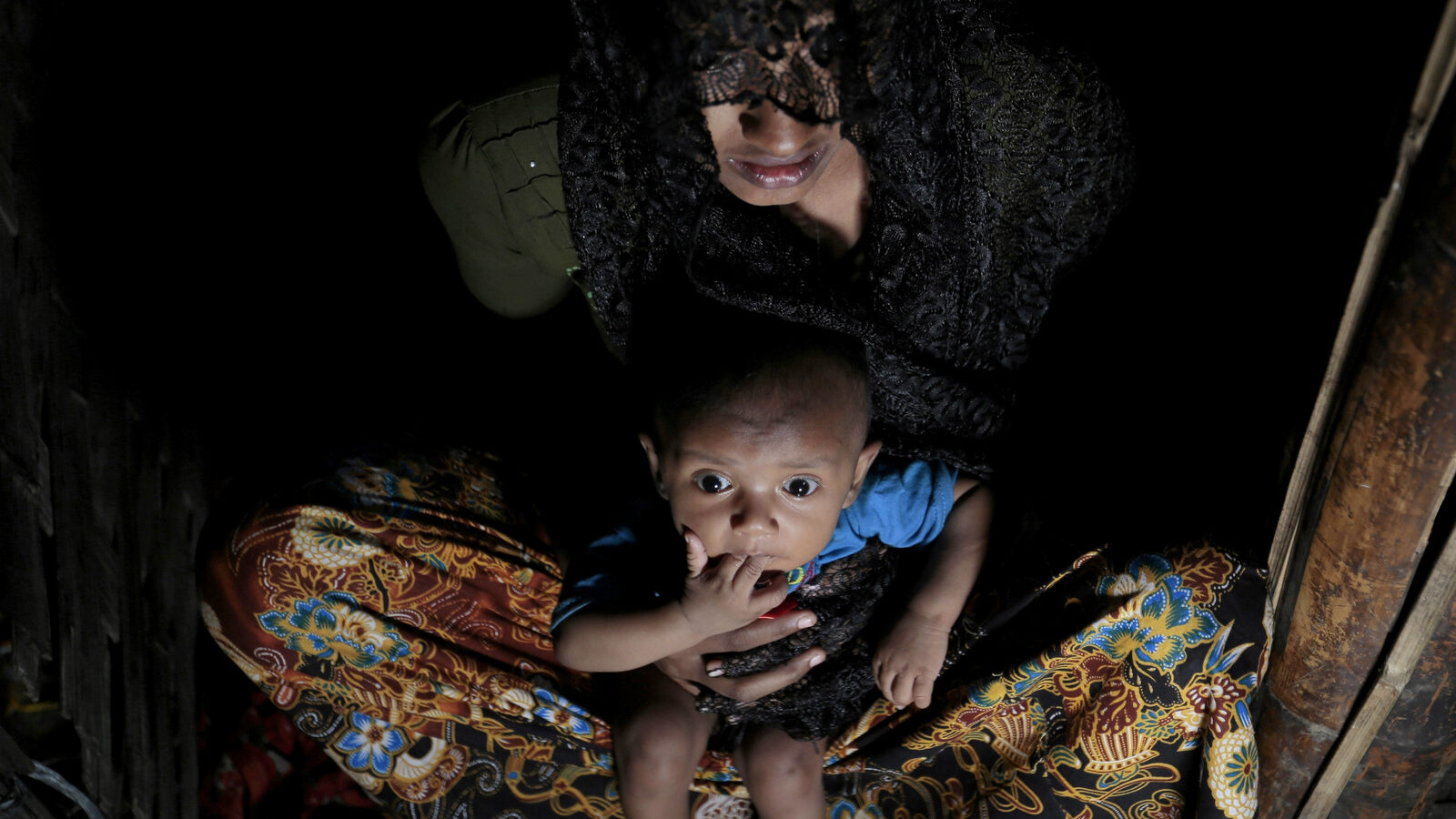 Mohsena Begum, a Rohingya who escaped to Bangladesh from Myanmar, holds her child and sits at the entrance of a room of an unregistered refugee camp in Teknaf, near Cox's Bazar, a southern coastal district about, 296 kilometers (183 miles) south of Dhaka, Bangladesh. Dec. 2, 2016. (AP Photo/A.M. Ahad)