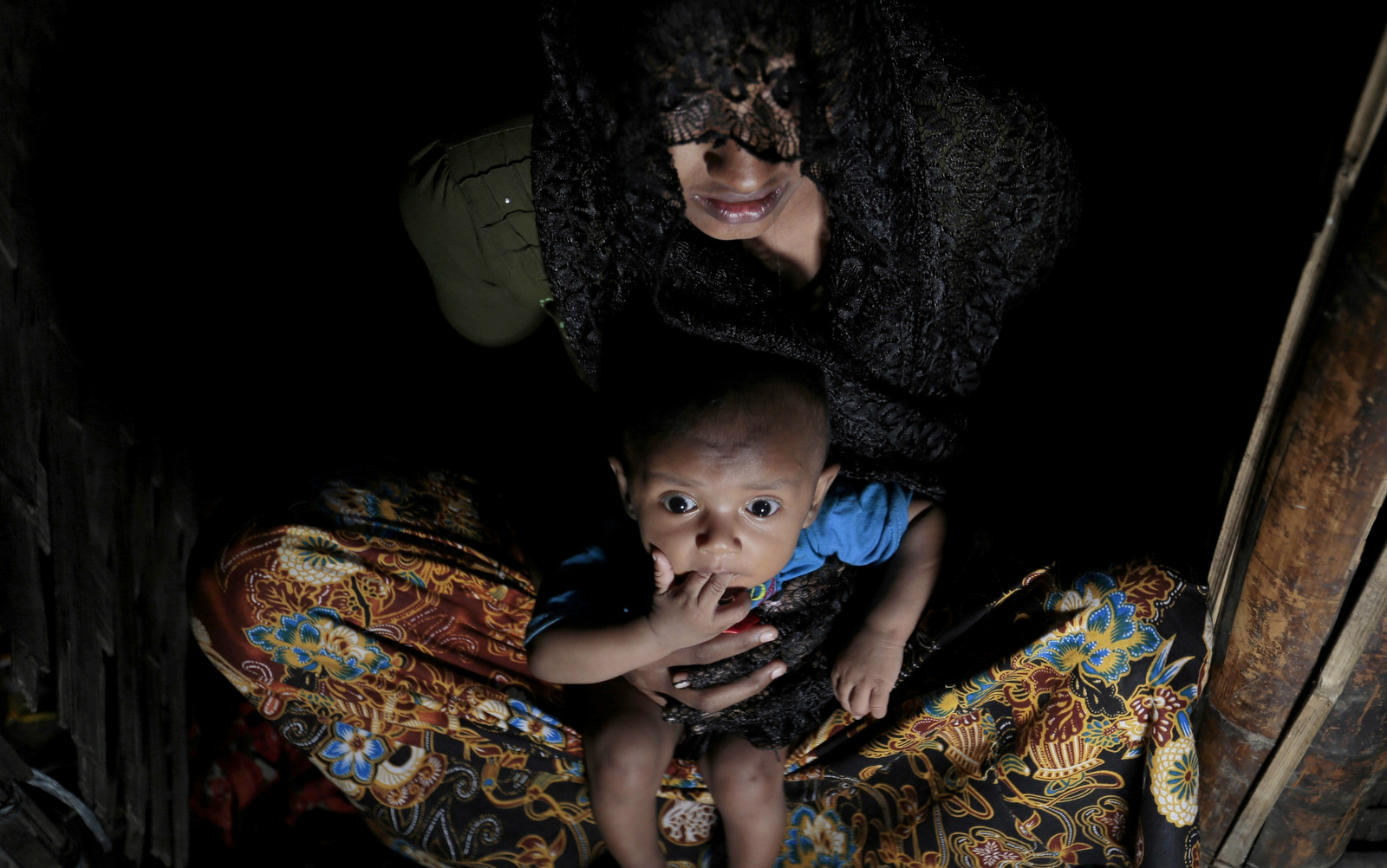 Mohsena Begum, a Rohingya who escaped to Bangladesh from Myanmar, holds her child and sits at the entrance of a room of an unregistered refugee camp in Teknaf, near Cox's Bazar, a southern coastal district about, 296 kilometers (183 miles) south of Dhaka, Bangladesh. Dec. 2, 2016. (AP Photo/A.M. Ahad)