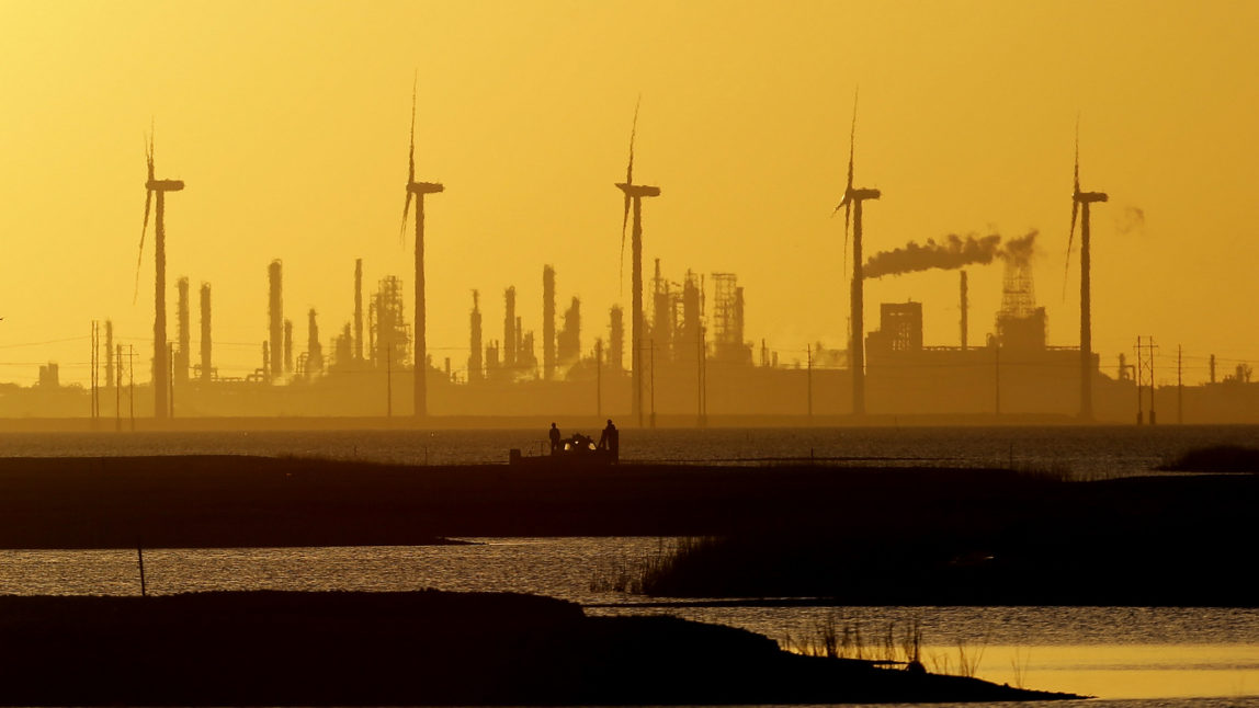Boaters pass through a channel as the sun set behind wind mills and an oil refinery, Tuesday, Jan. 14, 2014, in Corpus Christi, Texas. (AP Photo/Eric Gay)