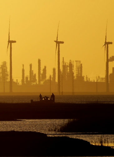 Boaters pass through a channel as the sun set behind wind mills and an oil refinery, Tuesday, Jan. 14, 2014, in Corpus Christi, Texas. (AP Photo/Eric Gay)