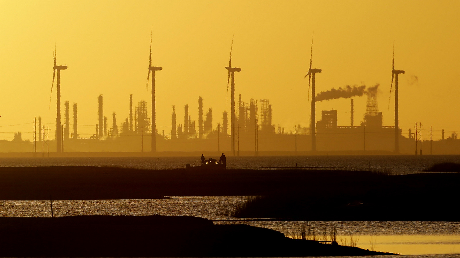 Boaters pass through a channel as the sun set behind wind mills and an oil refinery, Tuesday, Jan. 14, 2014, in Corpus Christi, Texas. (AP Photo/Eric Gay)