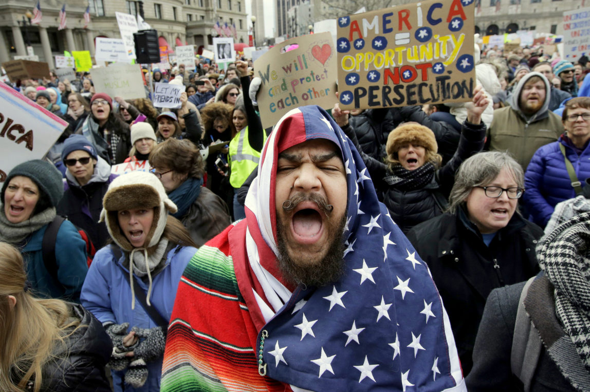 Izzy Berdan, of Boston, center, wears an American flags as he chants slogans with other demonstrators during a rally against President Donald Trump's order that restricts travel to the U.S., Sunday, Jan. 29, 2017, in Boston. (AP/Steven Senne)