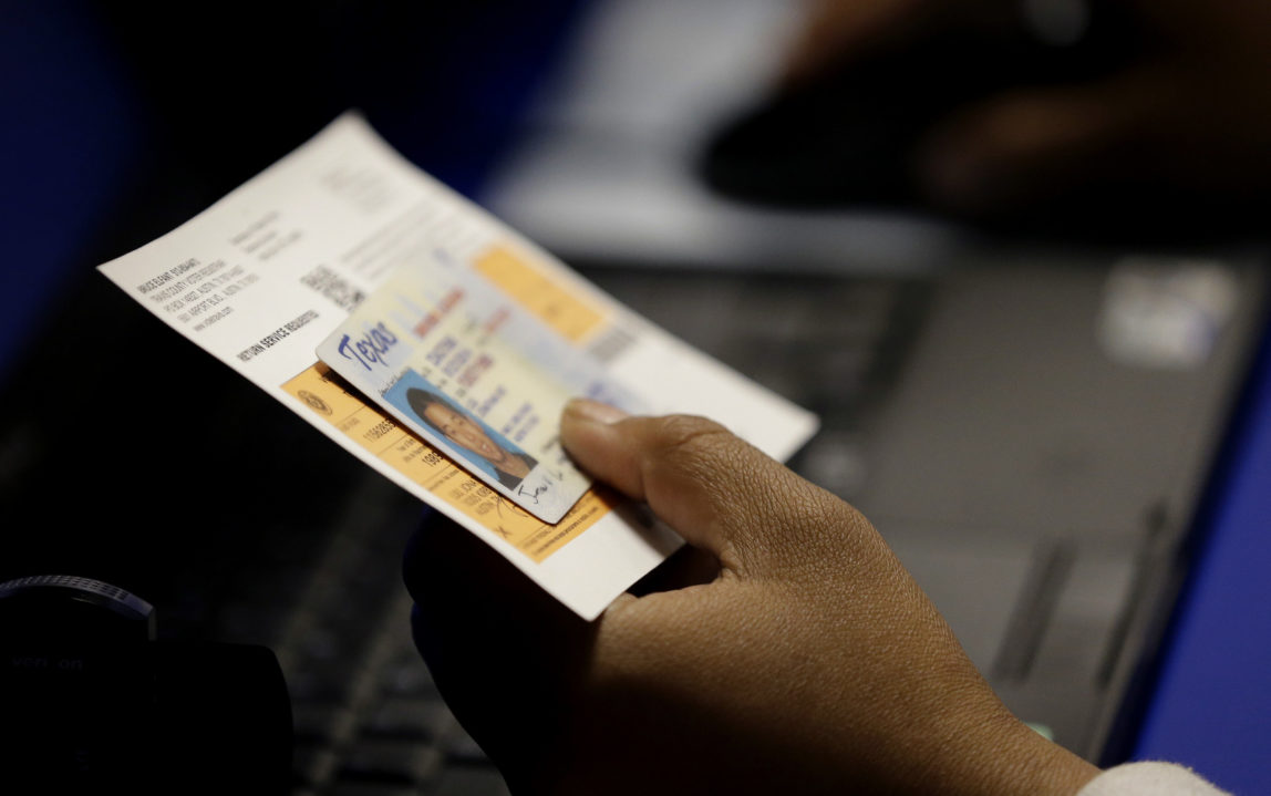 An election official checks a voter's photo identification at an early voting polling site in Austin, Texas. A federal appeals court is set to take a second look at a strict Texas voter ID law that was found to be unconstitutional last year. (AP/Eric Gay)