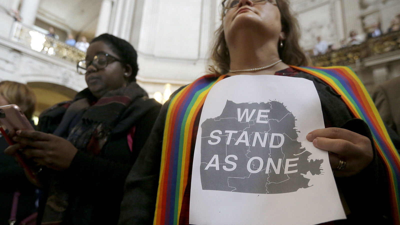 The Rev. Annie Steinberg-Behrman, right, provisional pastor with Metropolitan Community Church, holds a sign while listening to speakers at a meeting at City Hall in San Francisco by city leaders and community activists to reaffirm the city's commitment to being a sanctuary city in response to Donald Trump's support of deportations and other measures against immigrants Monday, Nov. 14, 2016. (AP Photo/Jeff Chiu)