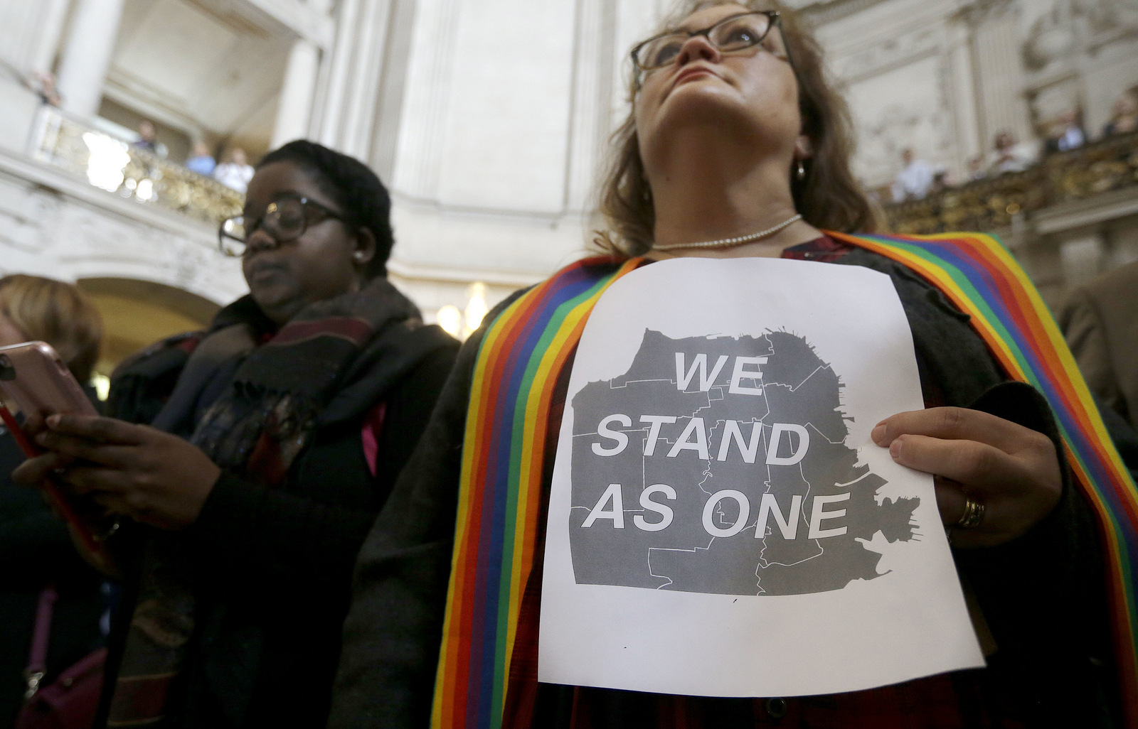 The Rev. Annie Steinberg-Behrman, right, provisional pastor with Metropolitan Community Church, holds a sign while listening to speakers at a meeting at City Hall in San Francisco by city leaders and community activists to reaffirm the city's commitment to being a sanctuary city in response to Donald Trump's support of deportations and other measures against immigrants Monday, Nov. 14, 2016. (AP Photo/Jeff Chiu)