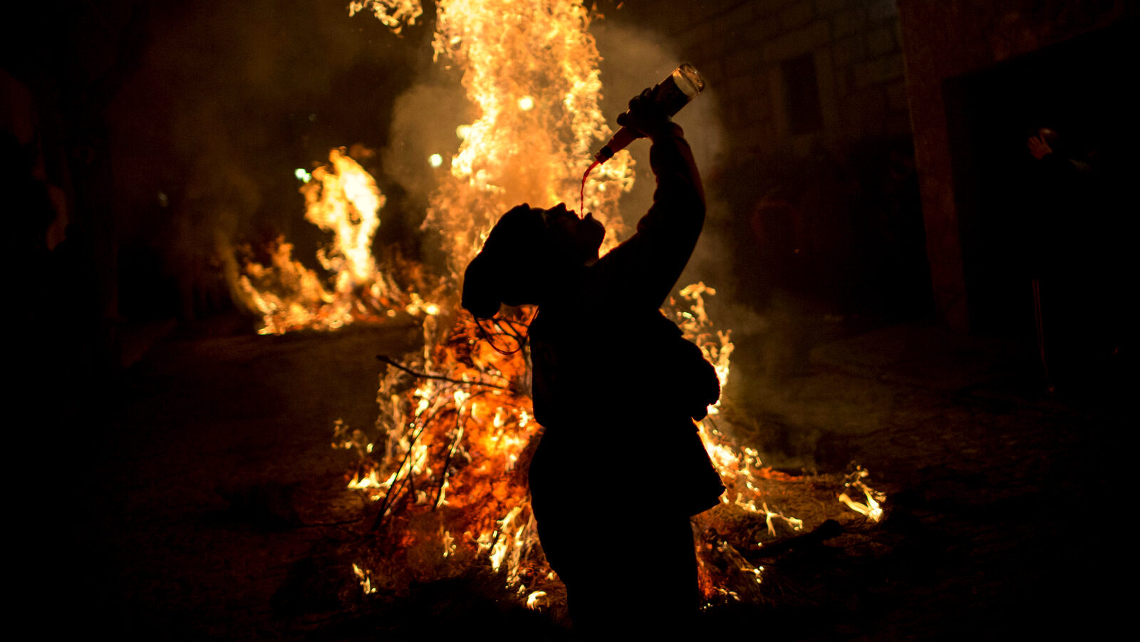 A woman drinks wine man next to a bonfire as part of a ritual in honor of Saint Anthony the Abbot, the patron saint of domestic animals, in San Bartolome de Pinares, about 100 km west of Madrid, Spain on Monday, Jan. 16, 2017. On the eve of Saint Anthony's Day, hundreds ride their horses through the narrow cobblestone streets of the small village of San Bartolome during the "Luminarias," a tradition that dates back 500 years and is meant to purify the animals with the smoke of the bonfires and protect them for the year to come. (AP Photo/Emilio Morenatti)