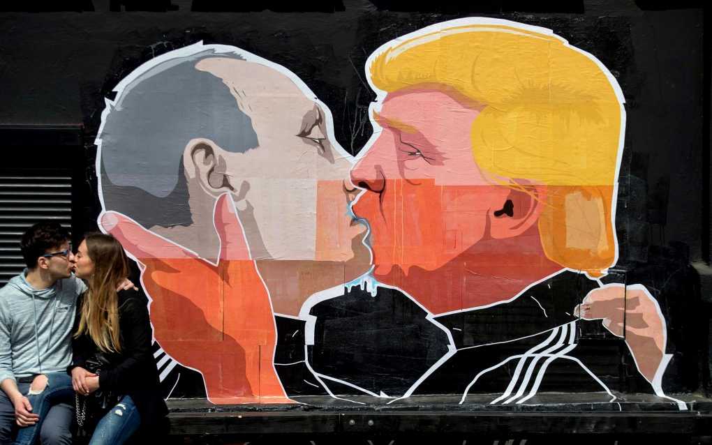 A couple kisses in front of graffiti depicting Russian President Vladimir Putin, left, and Republican presidential candidate Donald Trump, on the walls of a bar in the old town in Vilnius, Lithuania, Saturday, May 14, 2016. (AP Photo/Mindaugas Kulbis)