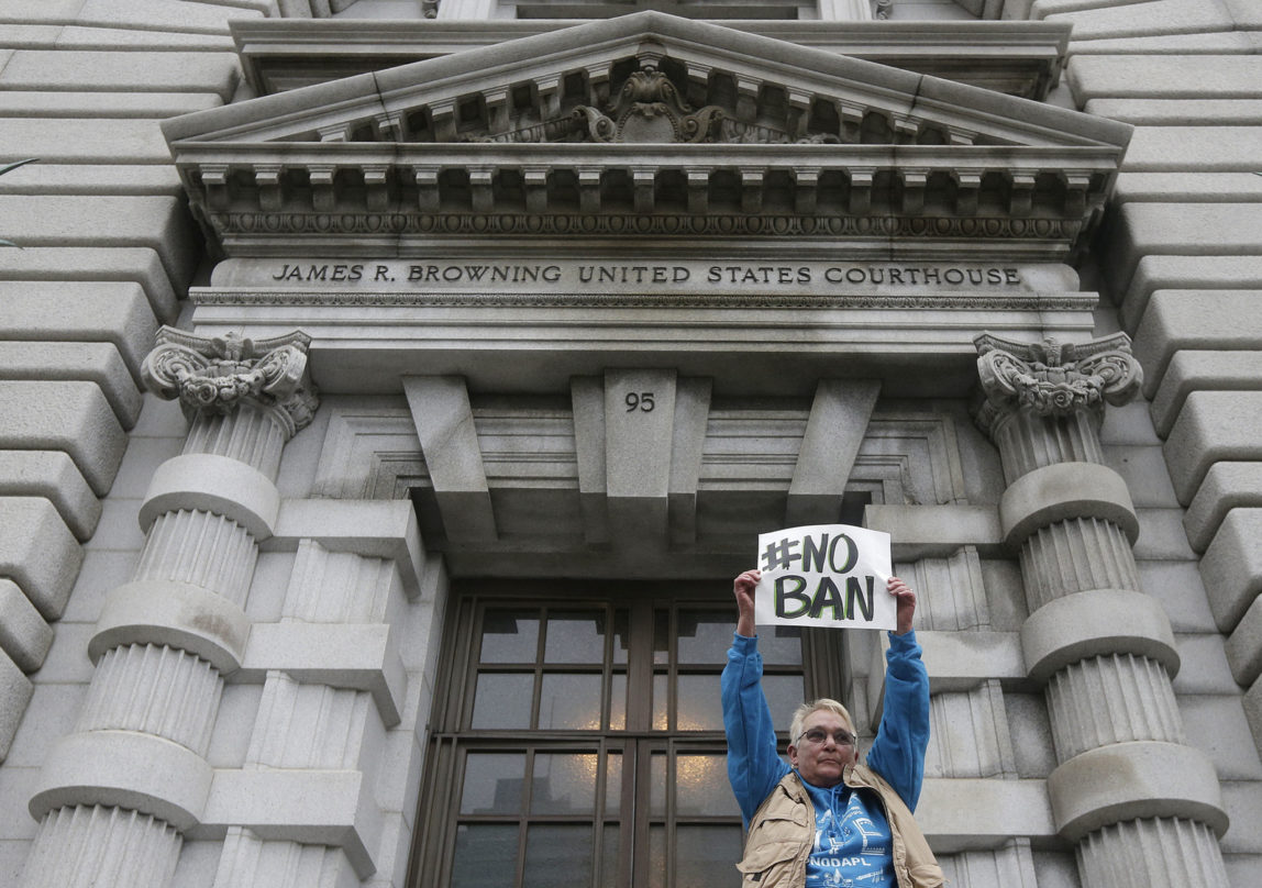 Karen Shore holds up a sign outside of the 9th U.S. Circuit Court of Appeals in San Francisco, Tuesday, Feb. 7, 2017. A panel of appeals court judges reviewing President Donald Trump's travel ban hammered away Tuesday at the federal government's arguments that the states cannot challenge the order. (AP/Jeff Chiu)