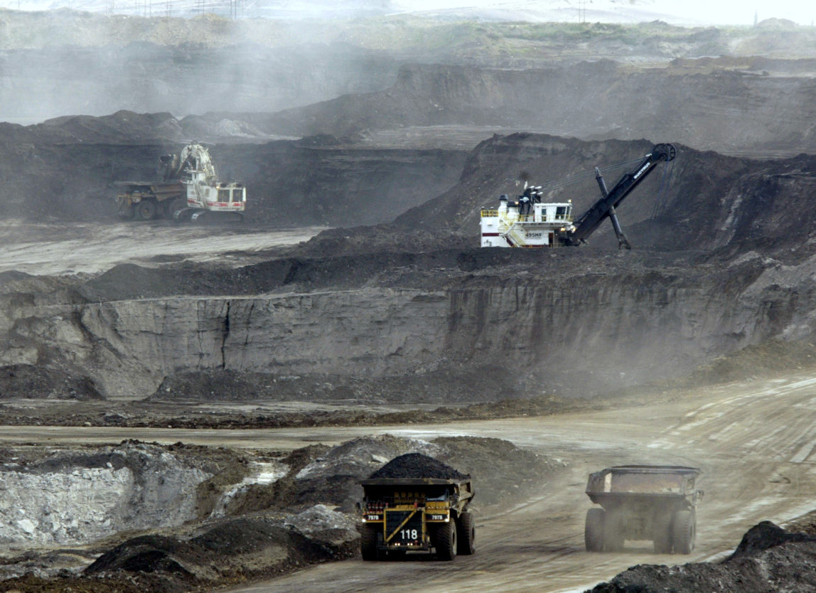 Mining trucks carry loads of oil laden sand after being loaded by huge shovels at the Albian Sands oils sands project in Ft. McMurray, Alberta, Canada. (AP/Jeff McIntosh)