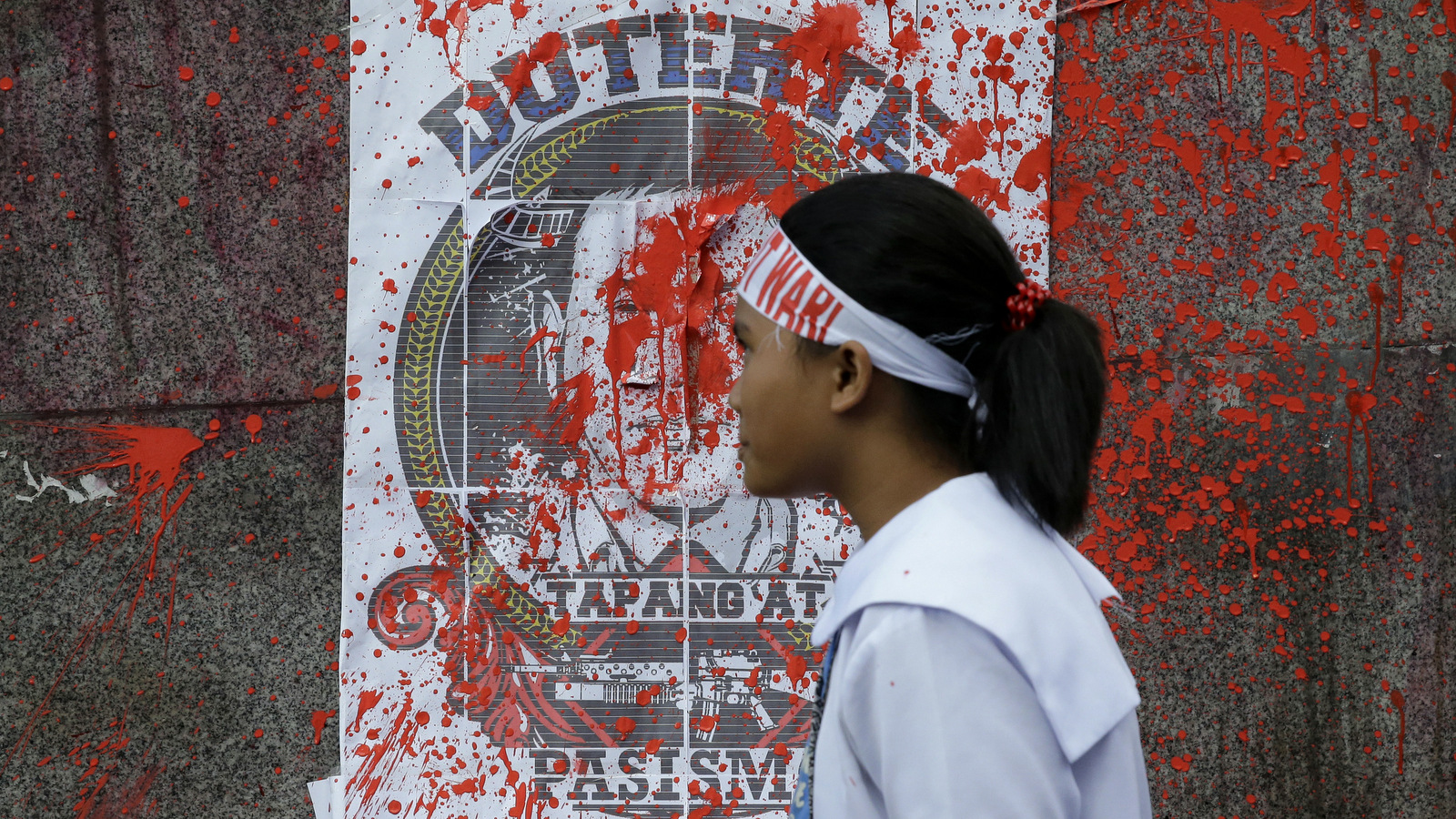 A Filipino student activist passes by a photo of Philippine President Rodrigo Duterte after red paint was thrown at it during a rally as they call for free education near the Malacanang presidential palace in Manila, Philippines, Thursday, Feb. 23, 2017. The group also denounced the alleged human rights violations by the military and police on activists. (AP/Aaron Favila)