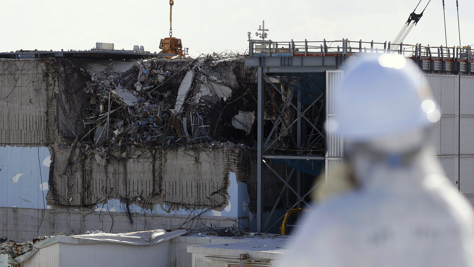 A member of the media tour group wearing a protective suit and a mask looks at the No. 3 reactor building at Tokyo Electric Power Co's (TEPCO) tsunami-crippled Fukushima Dai-ichi nuclear power plant in Okuma, Fukushima Prefecture, northeastern Japan, Wednesday, Feb. 10, 2016. (Toru Hanai/AP)