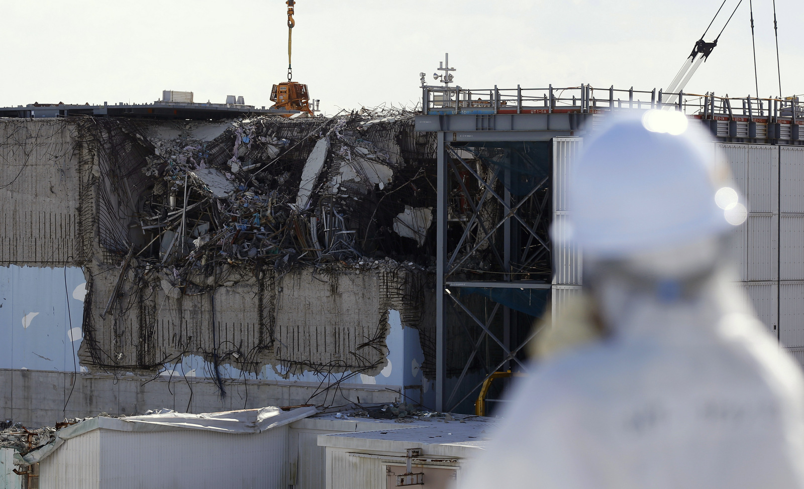 A member of the media tour group wearing a protective suit and a mask looks at the No. 3 reactor building at Tokyo Electric Power Co's (TEPCO) tsunami-crippled Fukushima Dai-ichi nuclear power plant in Okuma, Fukushima Prefecture, northeastern Japan, Wednesday, Feb. 10, 2016. (Toru Hanai/AP)