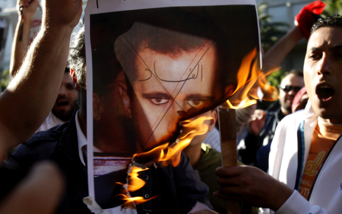 Anti-Assad protesters burn a picture of Syrian President Bashar al-Assad with 'Corruption' written across his face. (AP/Kostas Tsironis)