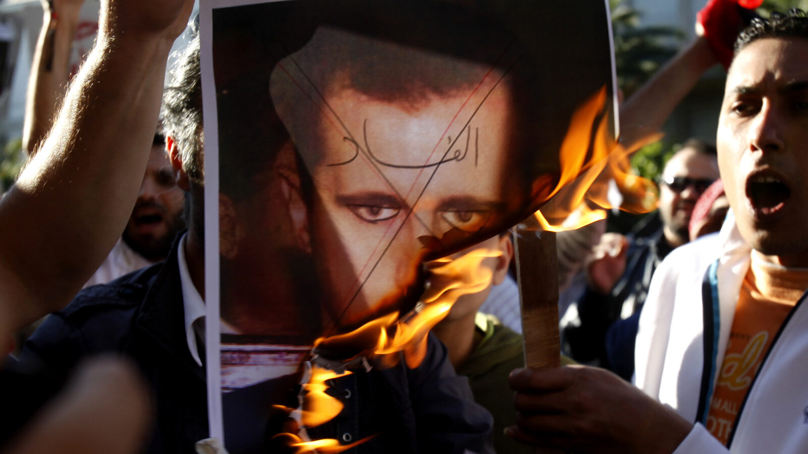 Anti-Assad protesters burn a picture of Syrian President Bashar al-Assad with 'Corruption' written across his face. (AP/Kostas Tsironis)