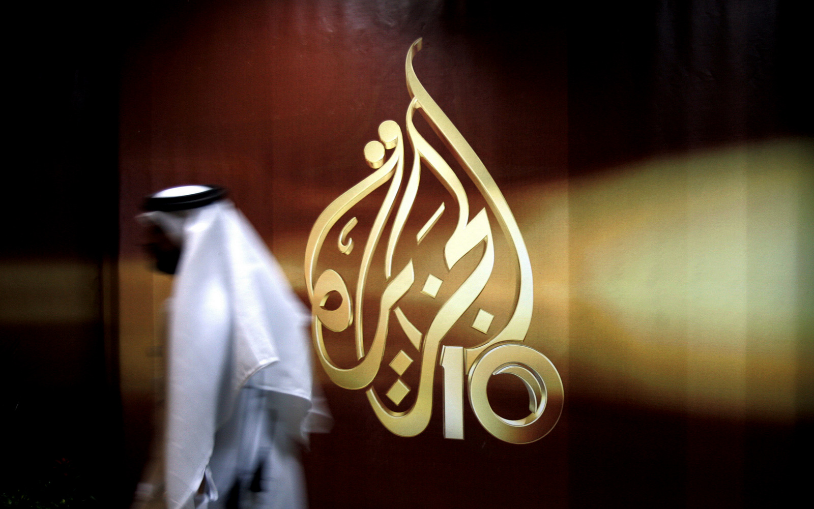 A Qatari employee of Al Jazeera Arabic language TV news channel walks past the logo of Al Jazeera in Doha, Qatar. (AP/Kamran Jebreili)