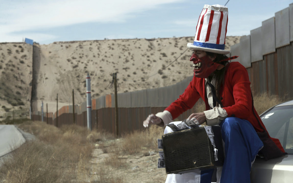 A protester dressed as a diabolical version of Uncle Sam holds a suitcase full of money at the U.S. border fence in Ciudad Juarez, Mexico, Sunday, Feb. 26, 2017. (AP/Christian Torres)