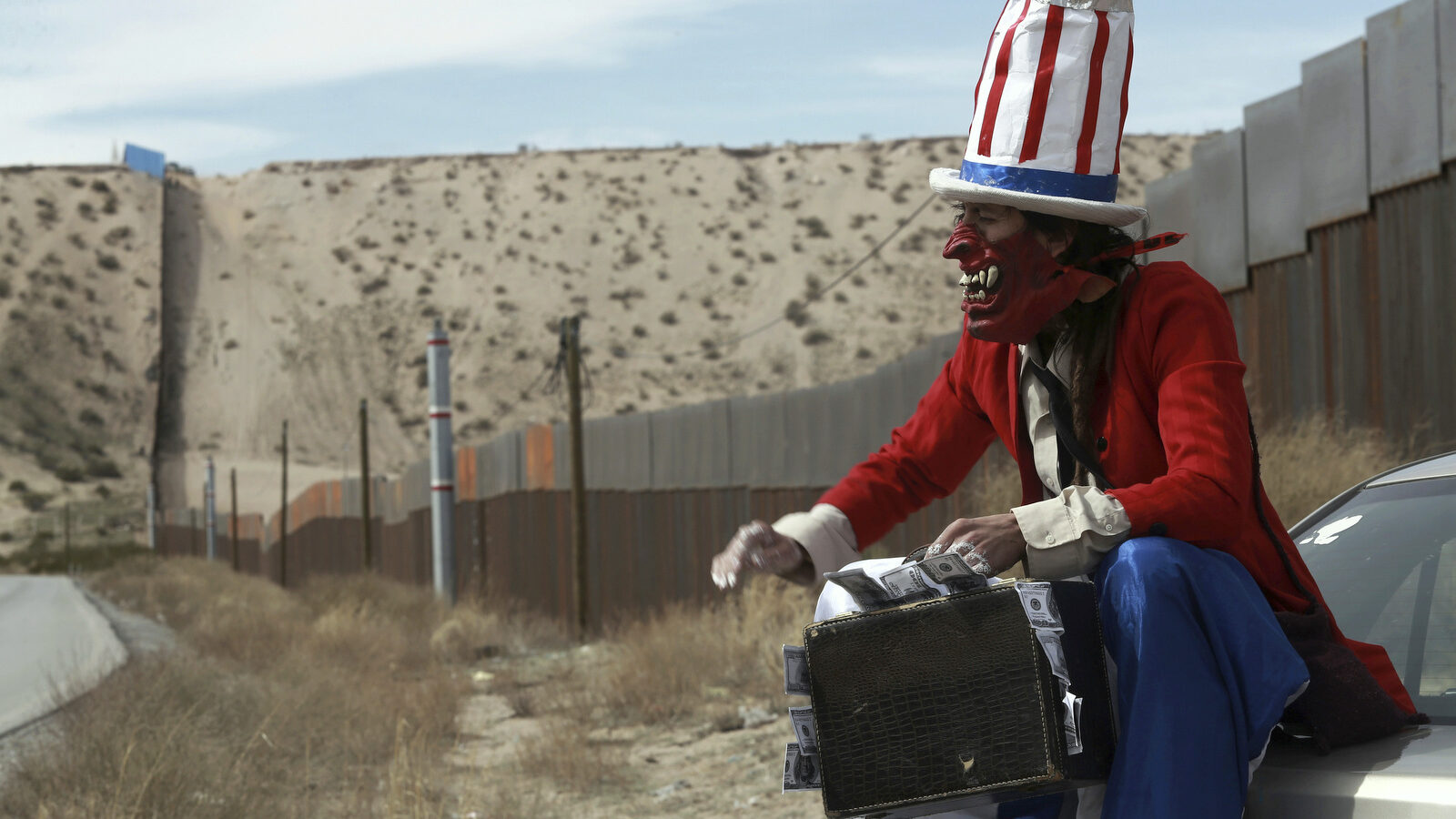 A protester dressed as a diabolical version of Uncle Sam holds a suitcase full of money at the U.S. border fence in Ciudad Juarez, Mexico, Sunday, Feb. 26, 2017. (AP/Christian Torres)