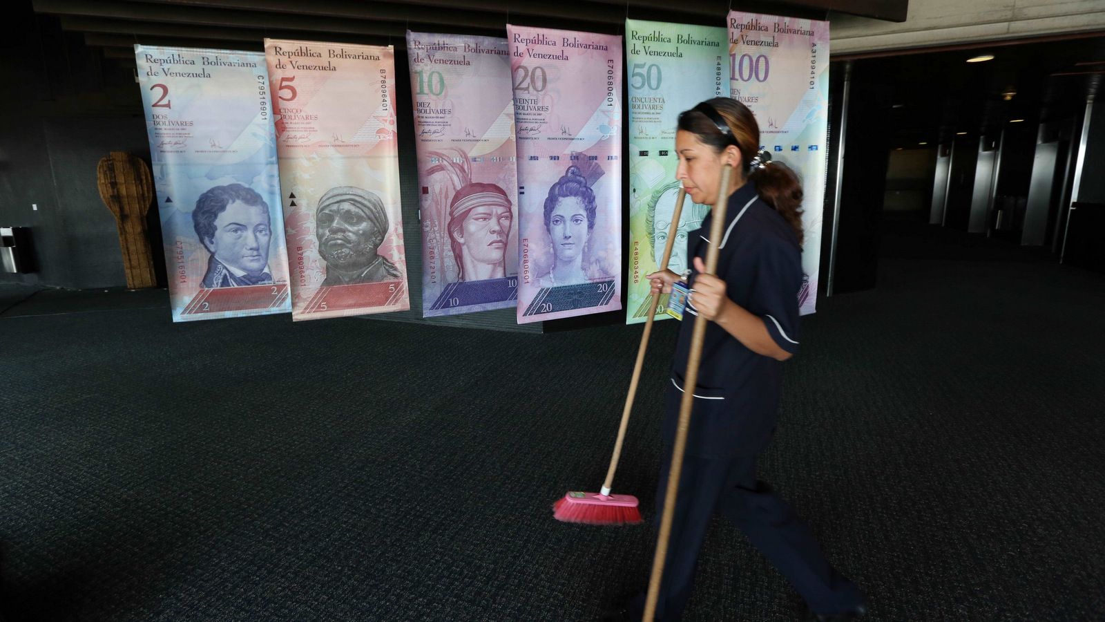 A cleaning woman walks by replicas of Venezuela's currency bills, hung in a hallway at the Central bank office building in Caracas, Venezuela. (AP/Ariana Cubillos)