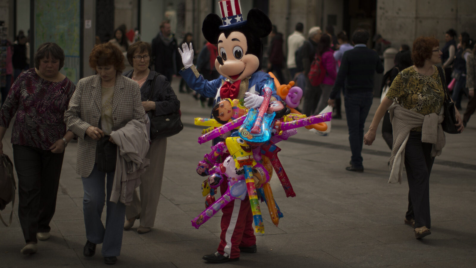 A man sells balloons wearing a Mickey Mouse costume with an US flag on his hat in a tourist area in Madrid, Spain. (AP/Andres Kudacki)