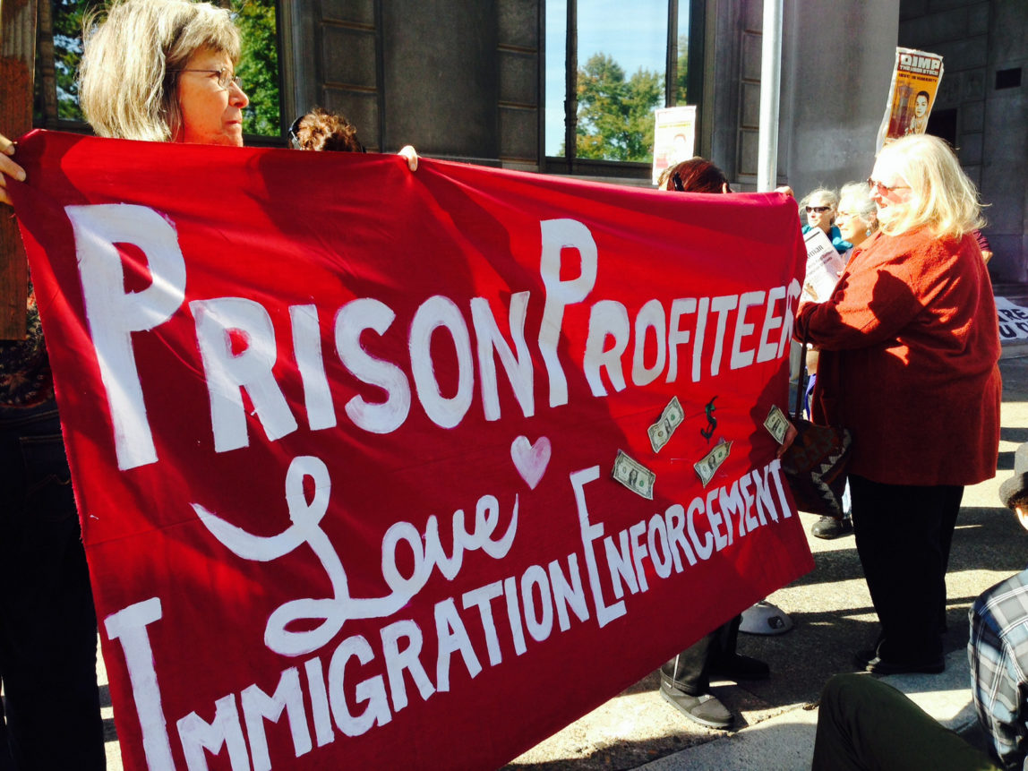 Immigration activists hold a banner while protesting the GEO Group which is one of the nation’s largest private prison companies and operator of multiple immigration detention centers. (AP/Gosia Wozniacka)