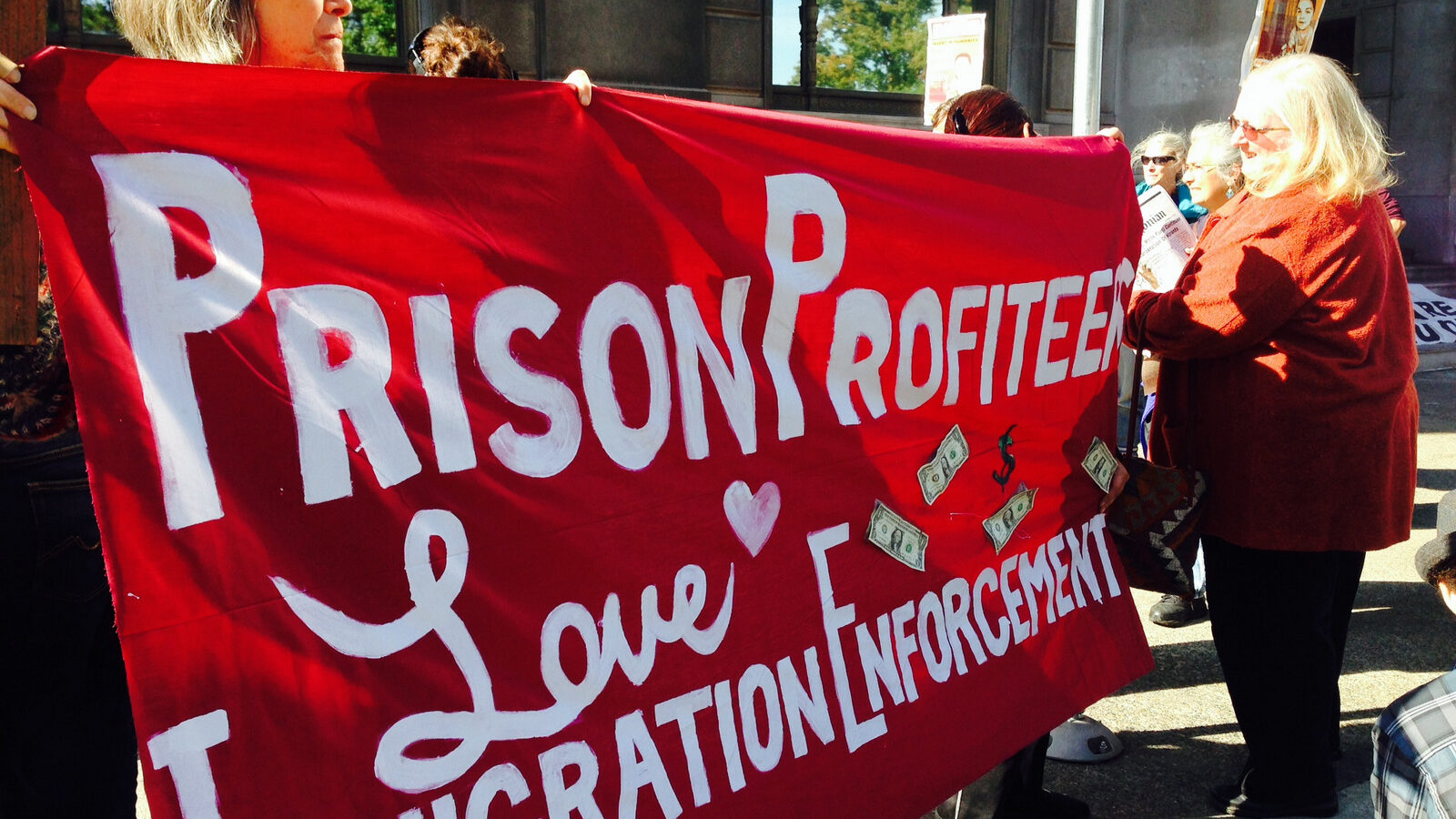 Immigration activists hold a banner while protesting the GEO Group which is one of the nation’s largest private prison companies and operator of multiple immigration detention centers. (AP/Gosia Wozniacka)