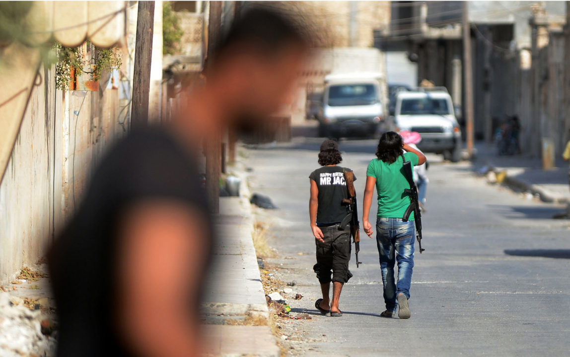 An unidentified man walks past young Free Syrian Army fighters patrolling the streets of Jarablus, Syria, Aug. 31, 2016. (Ismail Coskun/IHA/AP)