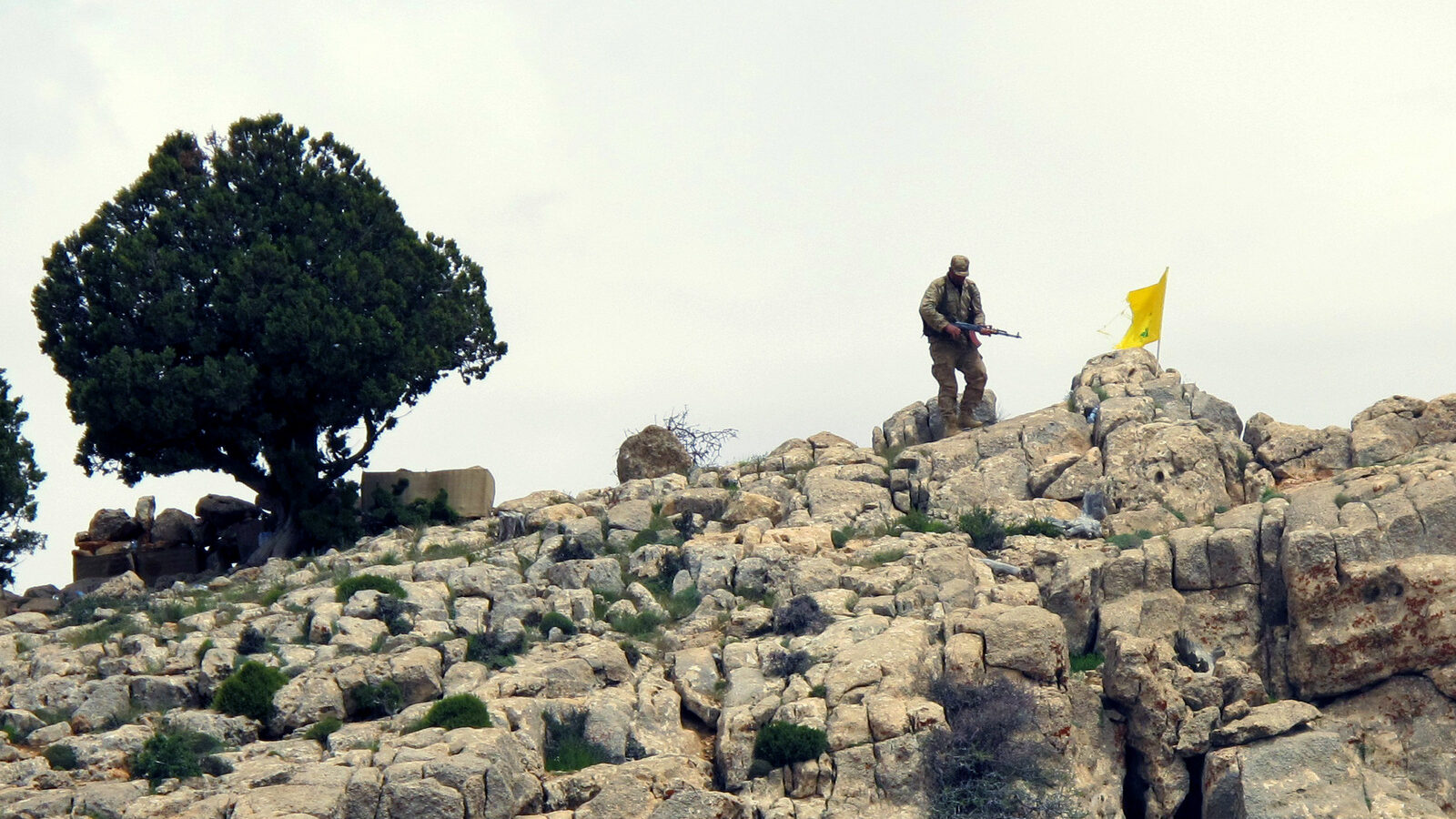 A Hezbollah fighter stands on a hill next to the group's yellow flag in the fields of the Syrian town of Assal al-Ward in the mountainous region of Qalamoun, Syria. (AP/Bassem Mroue)