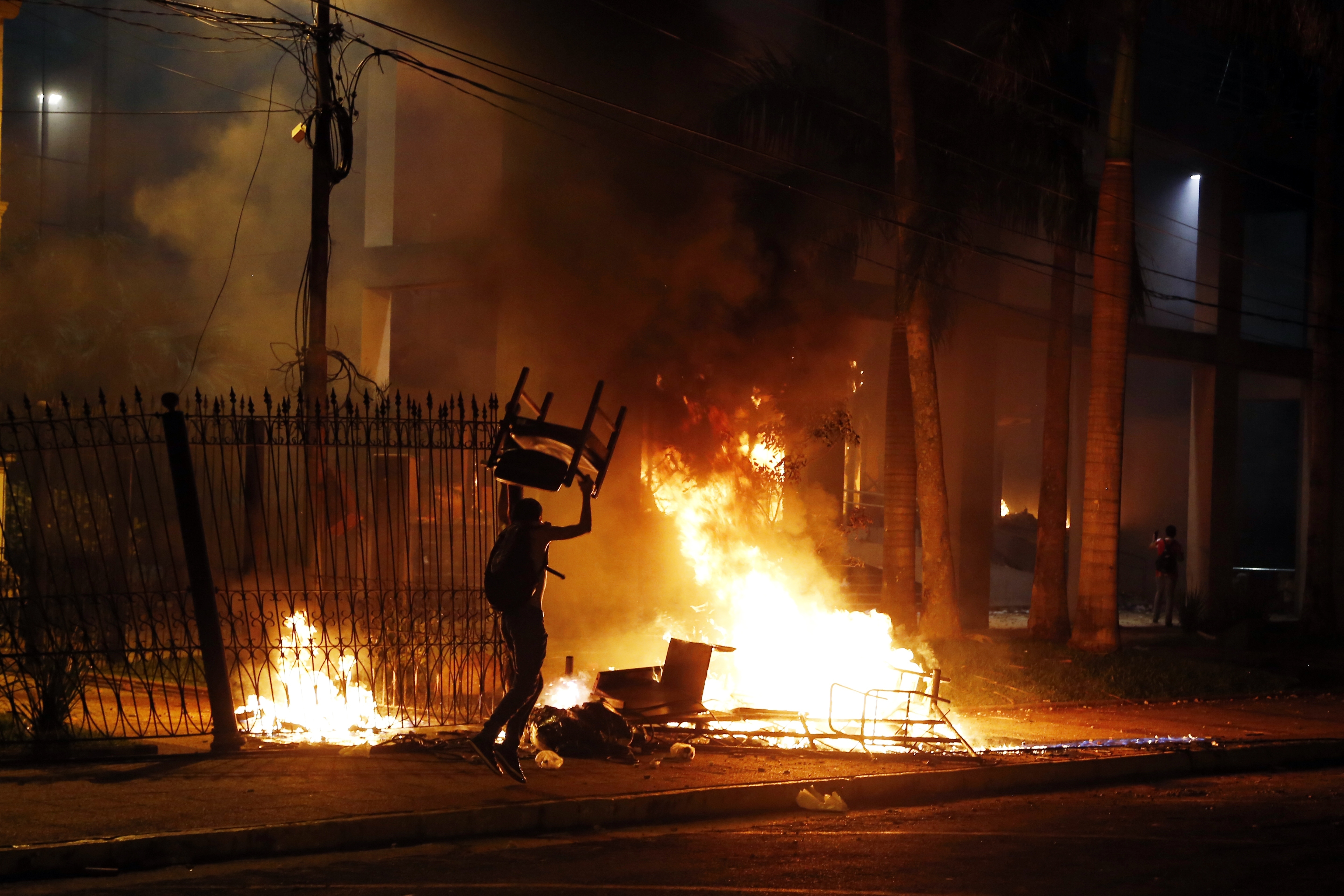 A protester carries a chair to a fire outside the congress building during clashes between police and protesters opposing an approved proposed constitutional amendment that would allow the election of a president to a second term, in Asuncion, Paraguay, Friday, March 31, 2017.  (AP/Jorge Saenz)