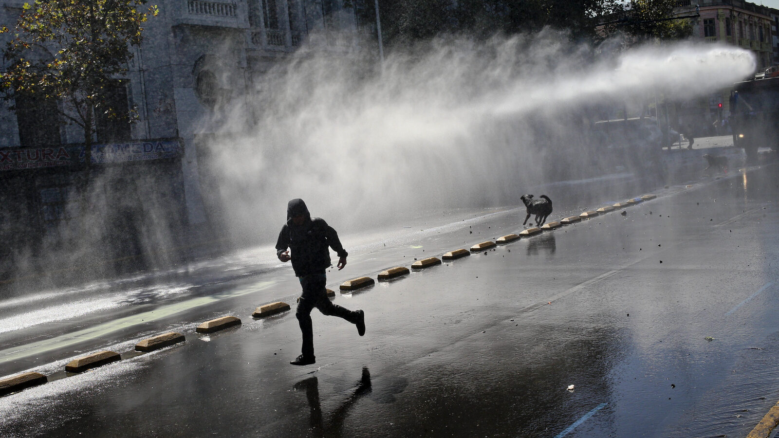 A demonstrator runs for cover as a police water cannon fires on them during a protest march demanding education reform, in Santiago, Chile, Tuesday, April 11, 2017. The demonstrators are demanding free access to school for all ages including at university level. (AP/Esteban Felix)