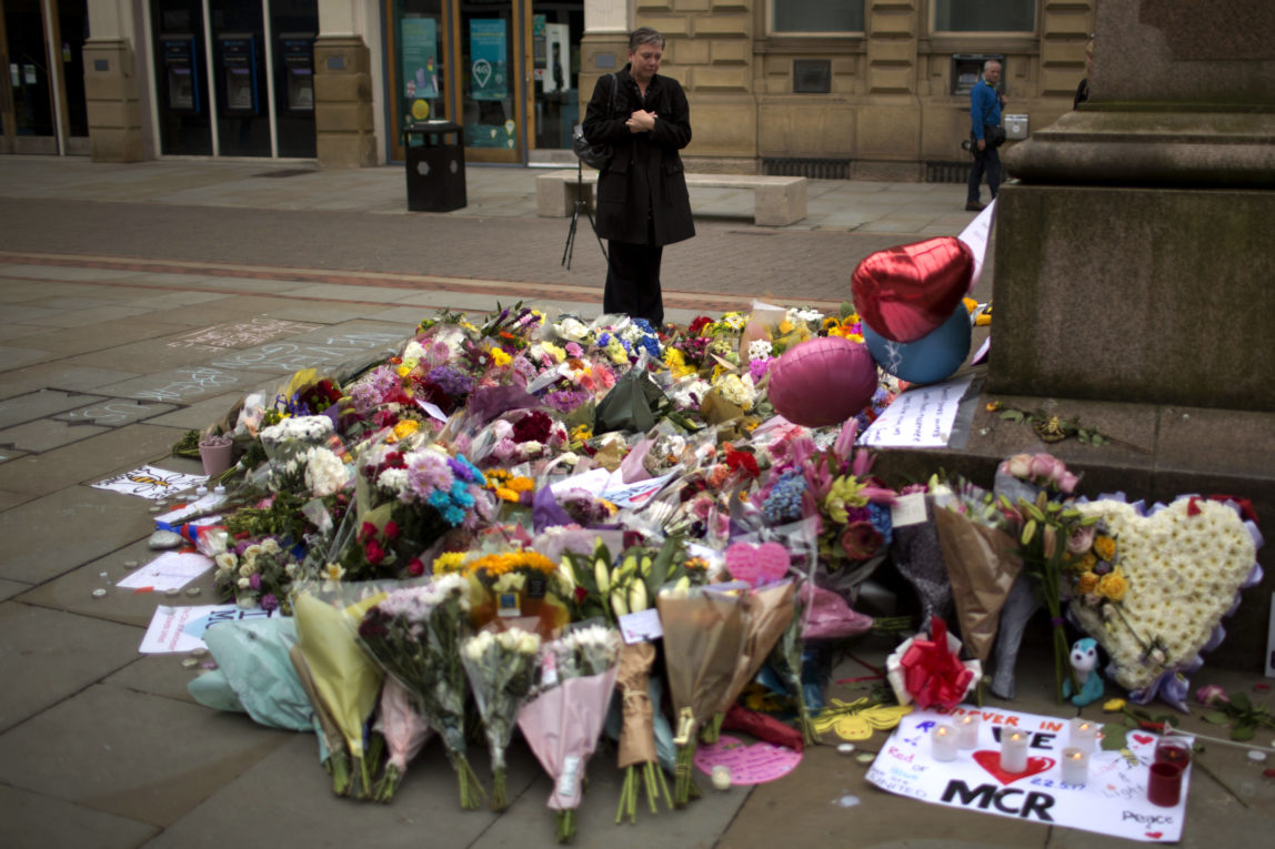 A woman stands next to flowers offered for the victims of a suicide attack at a concert by Ariana Grande that killed more than 20 people Monday night in central Manchester, Britain, May 24 2017. (AP/Emilio Morenatti)