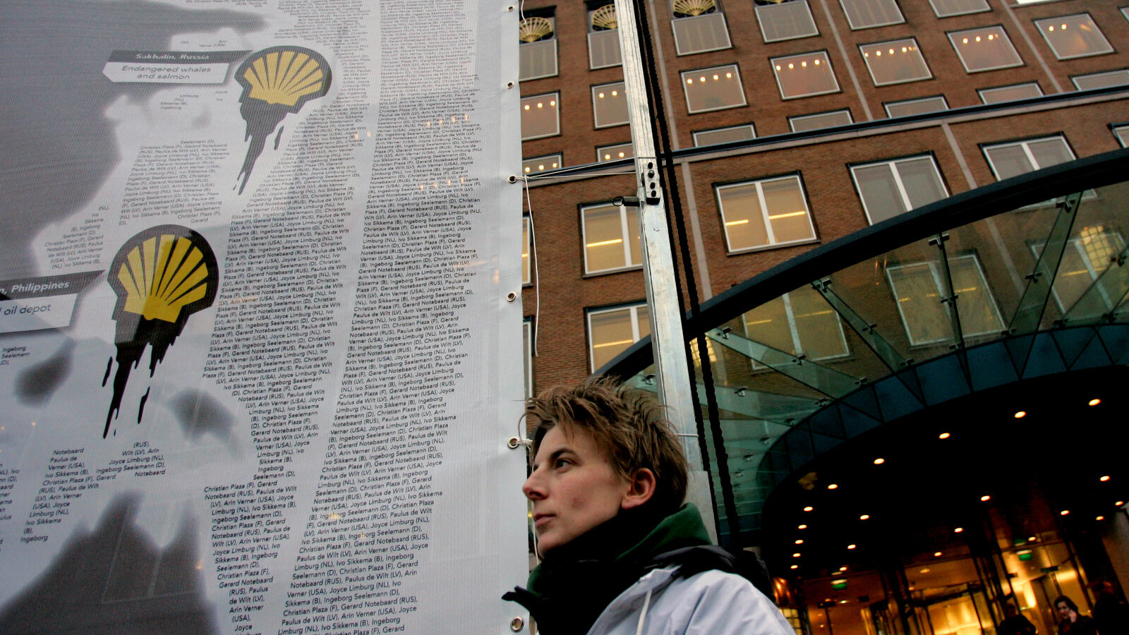 A demonstrator stands besides a banner with a Shell logo dripping oil, outside the Royal Dutch Shell PLC headquarters, rear, in The Hague, Netherlands. (AP/Peter Dejong)