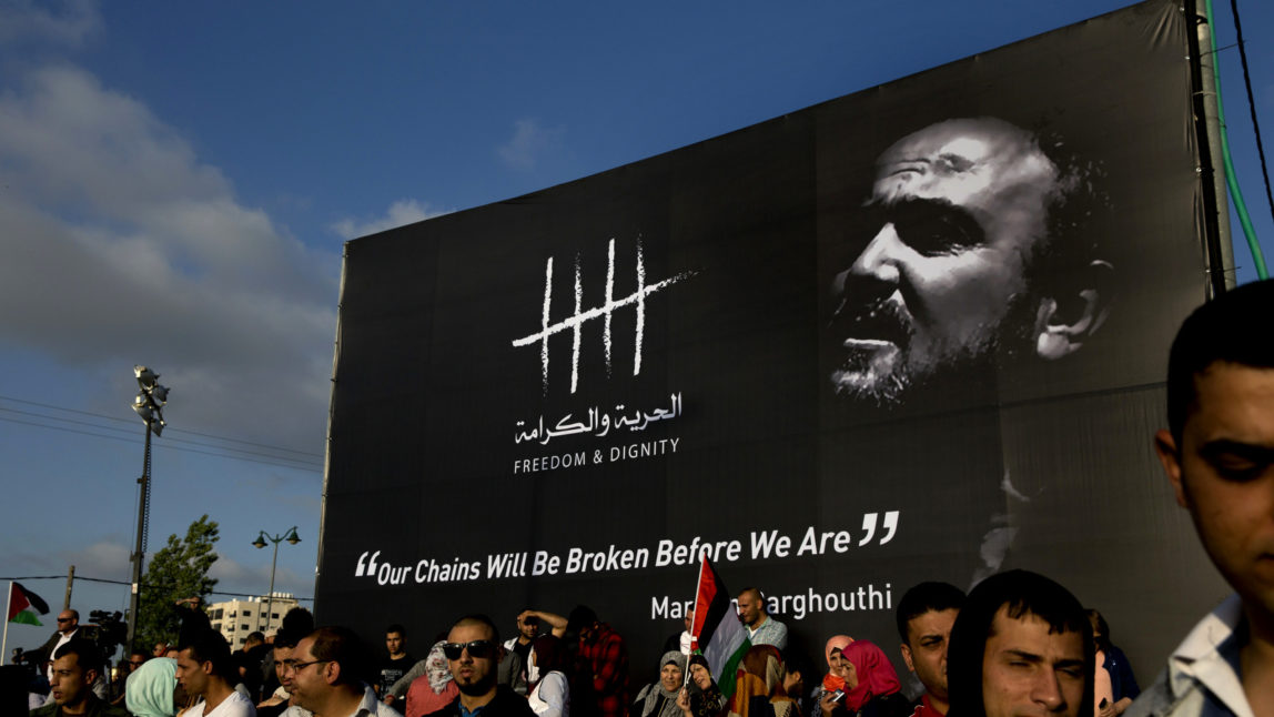 Protesters gather under a banner with a picture of jailed Palestinian uprising leader Marwan Barghouti during a rally supporting Palestinian prisoners in Israeli jails, who have been on an open-ended hunger strike in the West Bank city of Ramallah, May 3, 2017. The prisoners launched the protest to press for better conditions, including family visits. The International Committee of the Red Cross issued a rare statement, urging Israeli authorities to stop what it called the "systematic suspension" of family visits for the hunger strikers. (AP/Nasser Nasser)