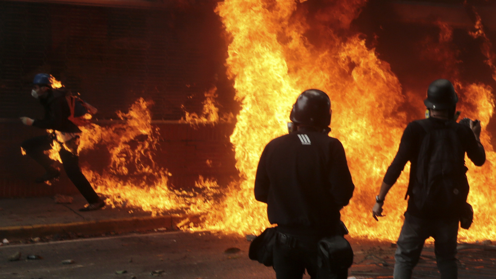 Anti-government protesters burn a Bolivarian National Guard motorbike, as one of them is covered in flames, left, during clashes with security forces blocking their march from reaching the National Assembly in Caracas, Venezuela, Wednesday, May 3, 2017. Driving the latest outrage is a decree by Venezuelan President Nicolas Maduro to begin the process of rewriting Venezuela's constitution, which was pushed through in 1999 by his predecessor and mentor, the late President Hugo Chavez. (AP/Fernando Llano)