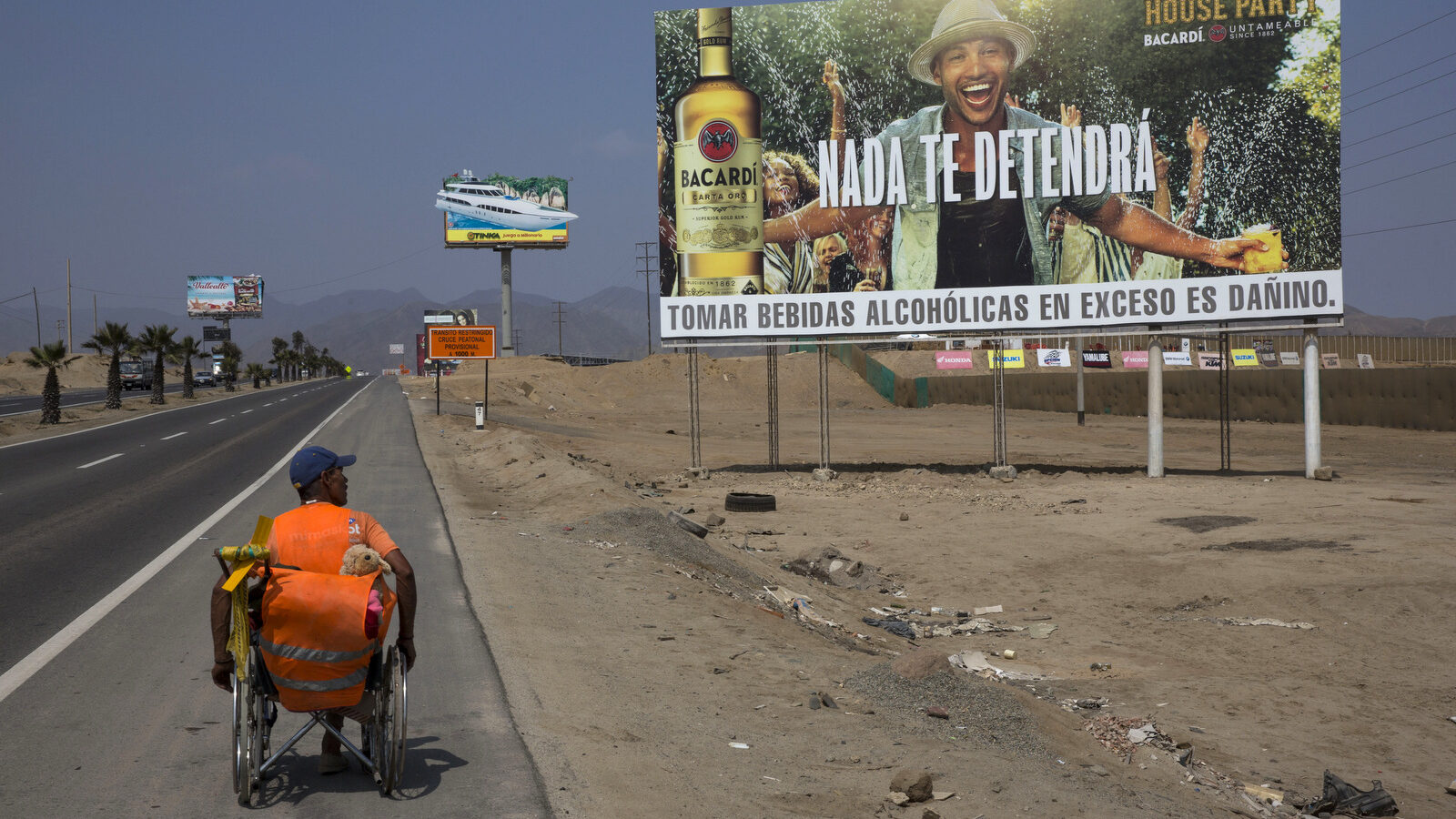 Jose Suarez, from Cucuta, Colombia, moves his wheelchair, decorated with a stuffed animal, along the Pan American Highway lined with billboards advertising rum, lottery and mixed nuts, on the south side of Lima, Peru. Suarez, 58, said he's on a mission to reach Brazil in his wheelchair, after leaving Cucuta in January. The billboard reads in Spanish "Nothing will stop you." (AP/Rodrigo Abd)