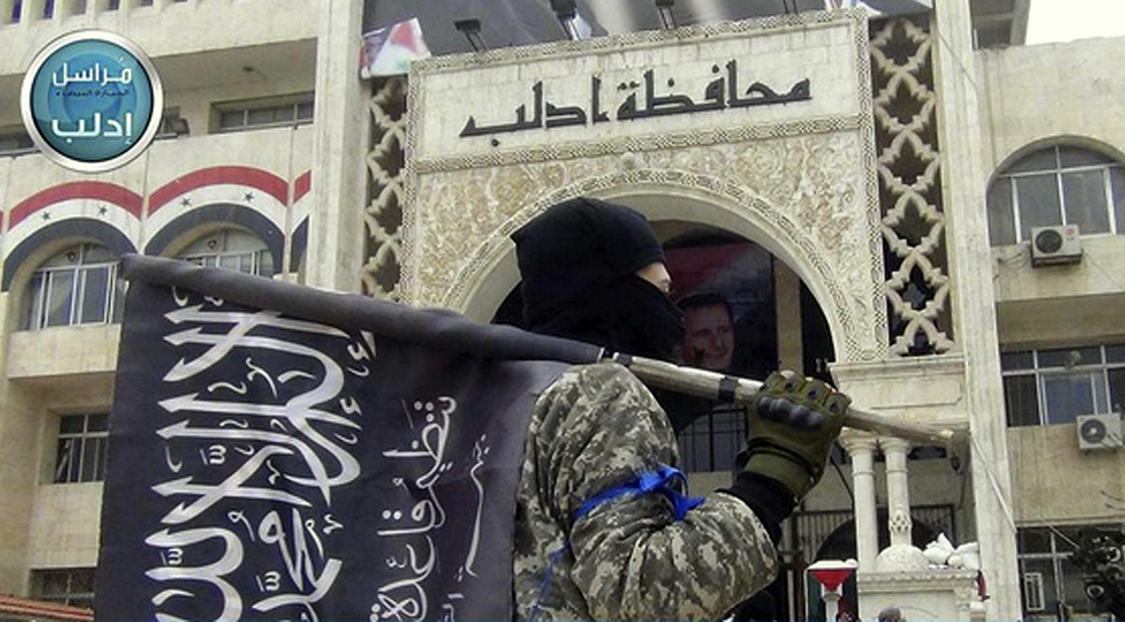 Un luchador de Nusra sostiene la bandera de su grupo mientras se encuentra frente al edificio del gobernador en la provincia de Idlib, en el norte de Siria. (Foto: Twitter vía AP)