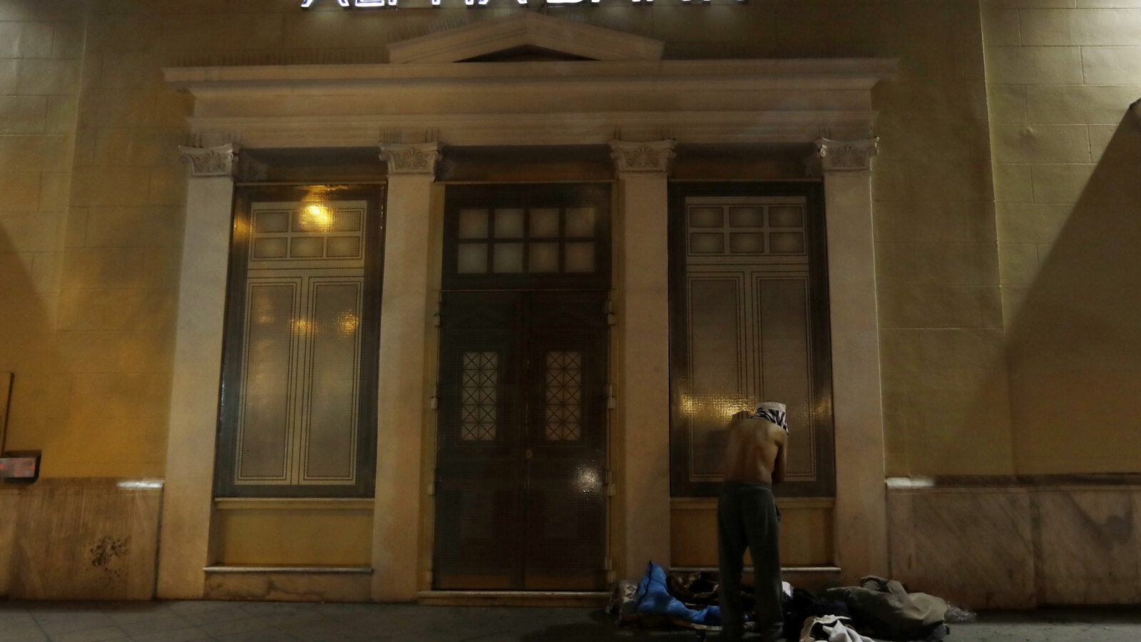 A homeless person changes clothes outside a bank in central Athens. Nearly one-in-four Greeks are unemployed and receive no benefits. Poverty rates have surged here since the start of the crisis in late 2009, with nearly 36 percent of the country living in financial distress. (AP/Thanassis Stavrakis)