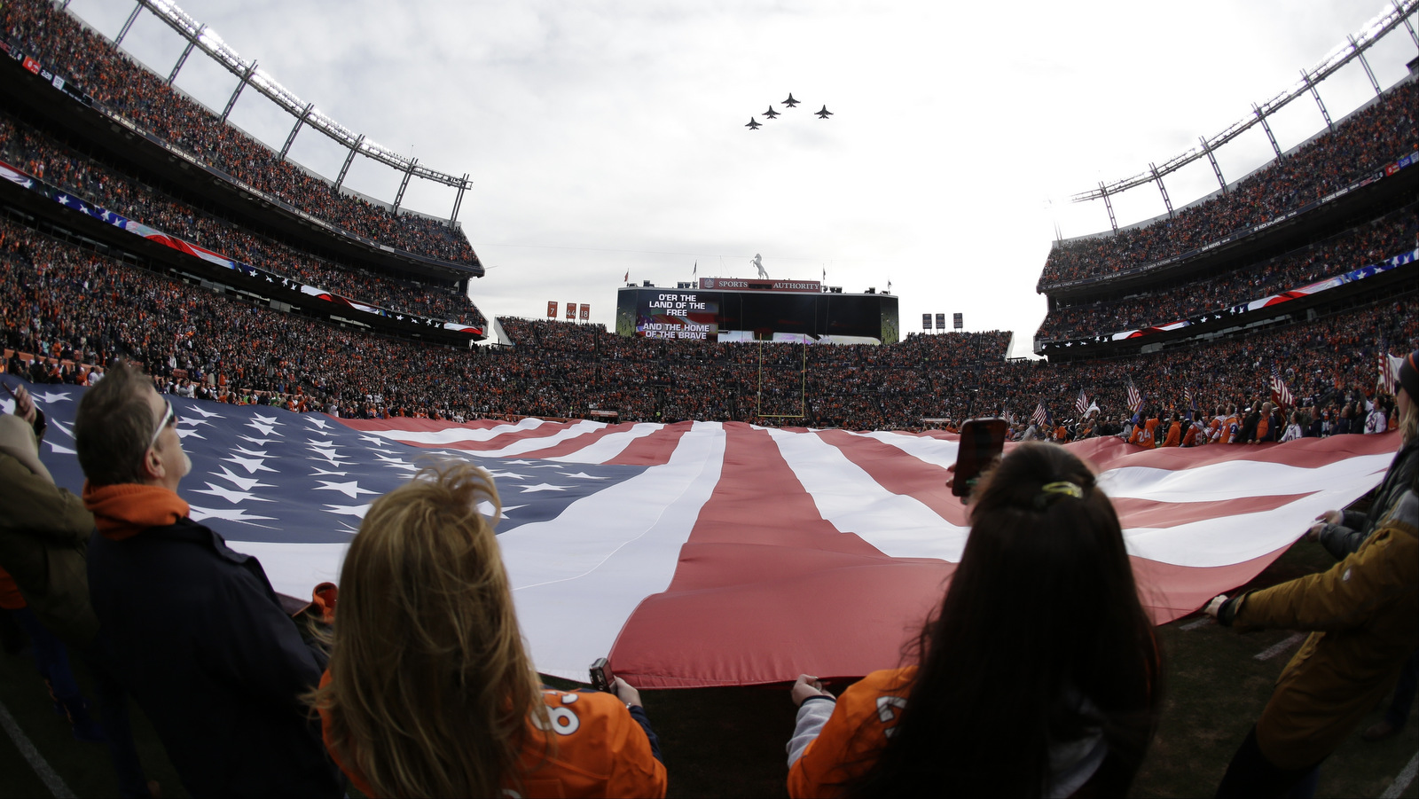 A giant U.S. flag is displayed during a military fly-over at Sports Authority Field at Mile High before an NFL football game between the Denver Broncos and the Oakland Raiders, Sunday, Jan. 1, 2017, in Denver. (AP/Jack Dempsey)