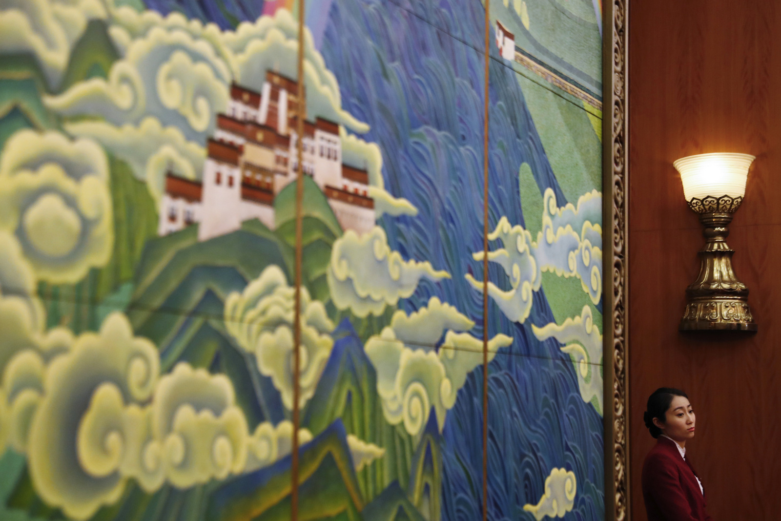 A tea hostess stands next to a mural depicting Tibet on display in the Tibet room in the Great Hall of the People during the Tibetan province delegation meeting held as part of the National People's Congress in Beijing, March 10, 2017. (AP/Andy Wong)